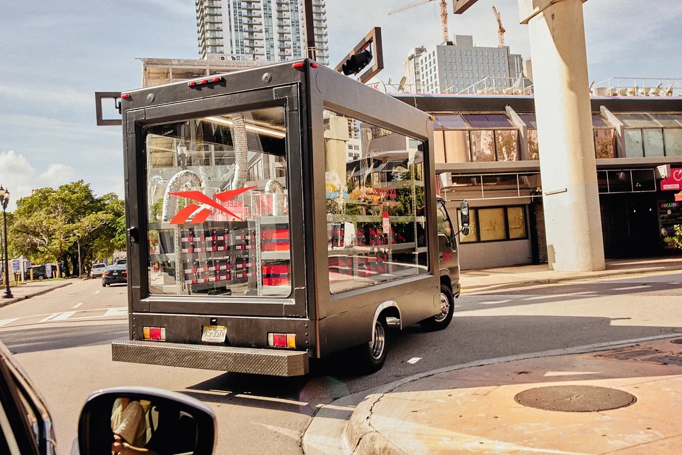 Black Reebok promotional truck with glass sides revealing shoe inventory driving through a sunny city street.