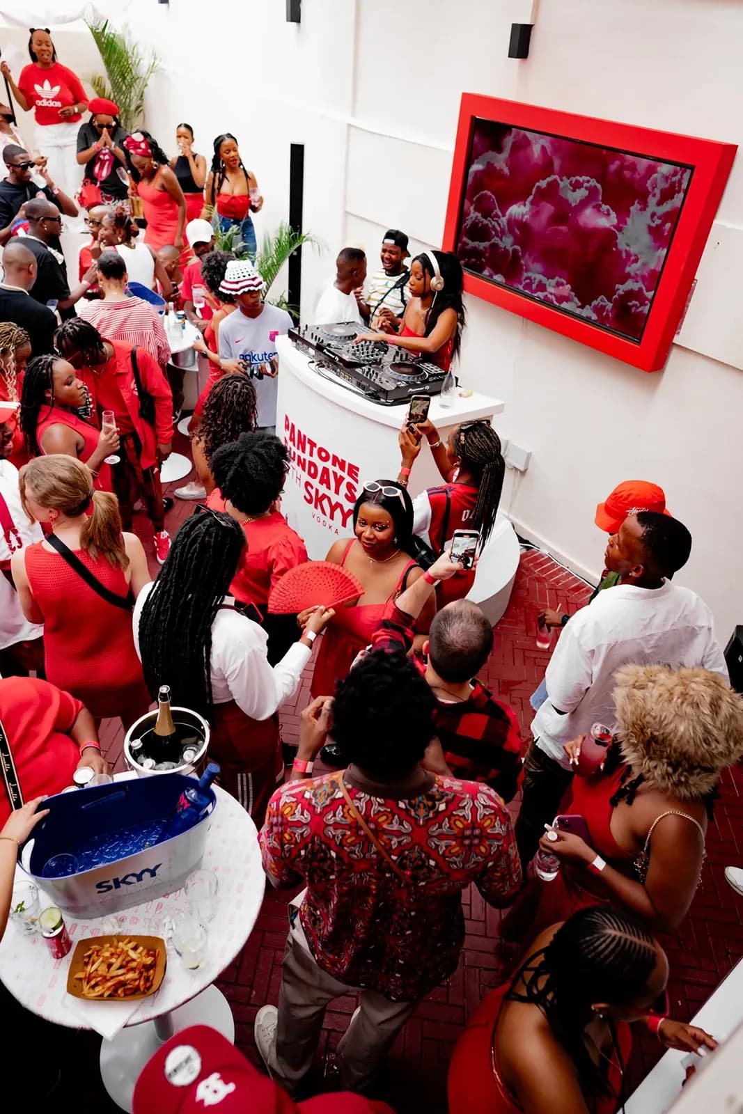 High-angle view of a crowded outdoor party with attendees in red outfits dancing near a white DJ booth.