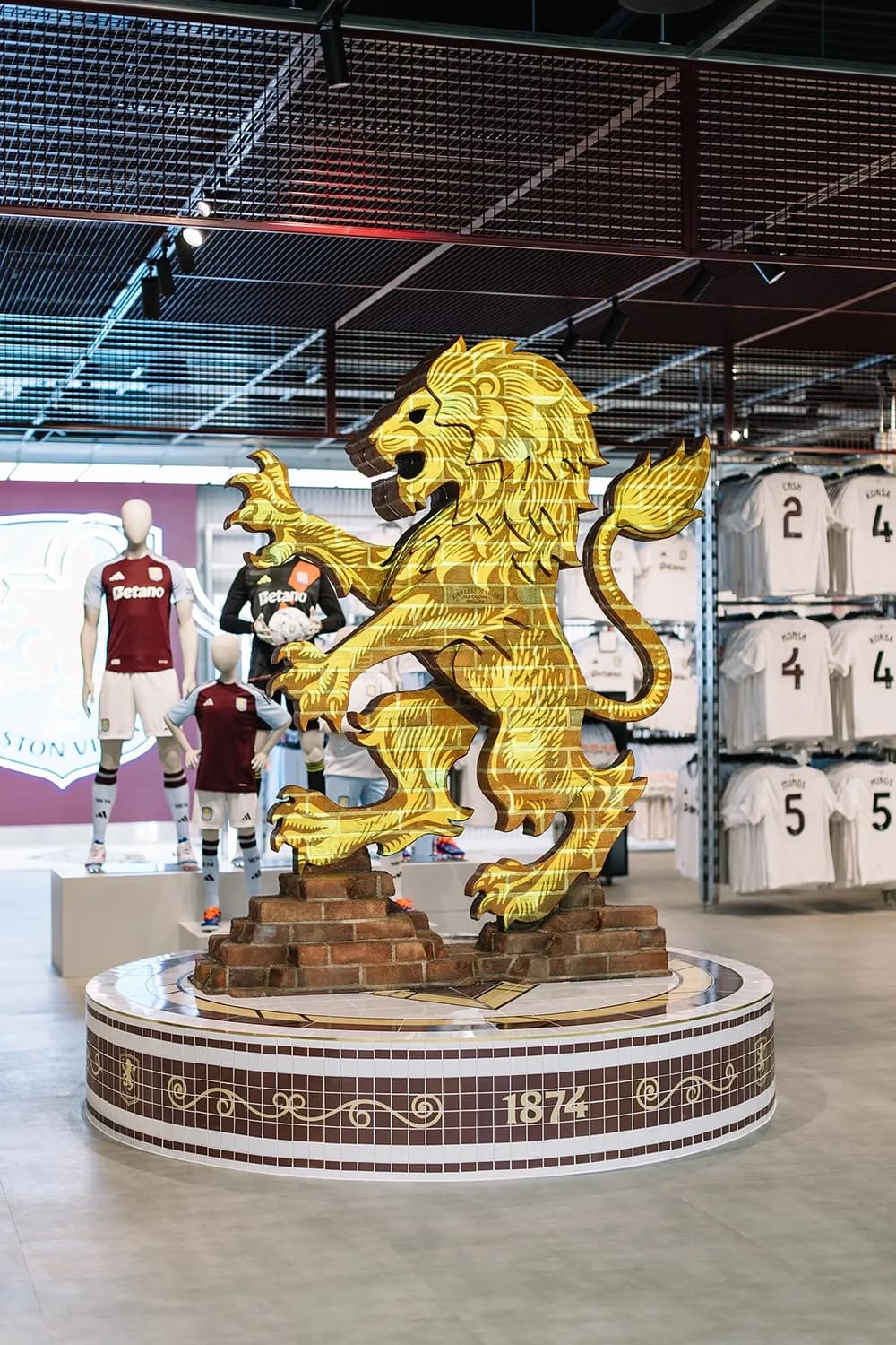 Large lion sculpture covered in a brick pattern featuring the Aston Villa crest, located in the center of the store.