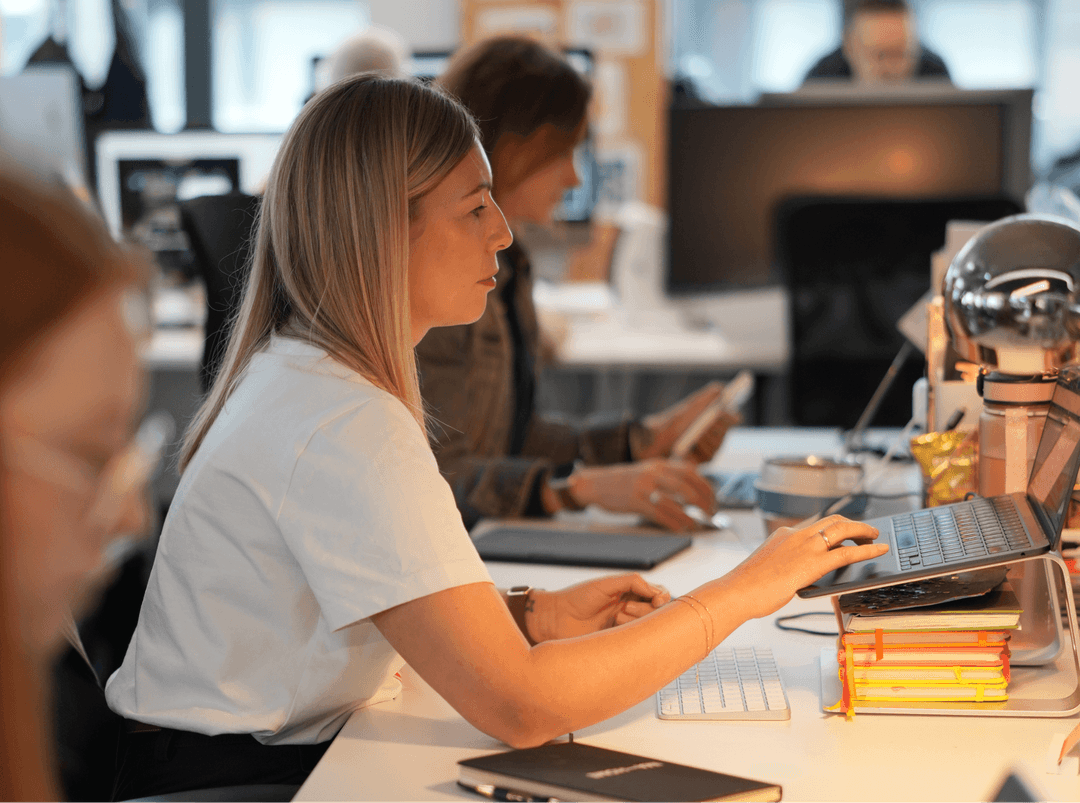 Two women sitting side-by-side working on laptops in a focused, collaborative office environment.