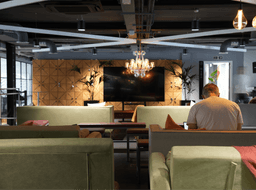 A stylish office lounge in Leeds with comfortable seating, a chandelier, and a large wall-mounted screen.