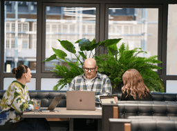 Colleagues sitting around a wooden table in a bright, modern London office with lush indoor plants.