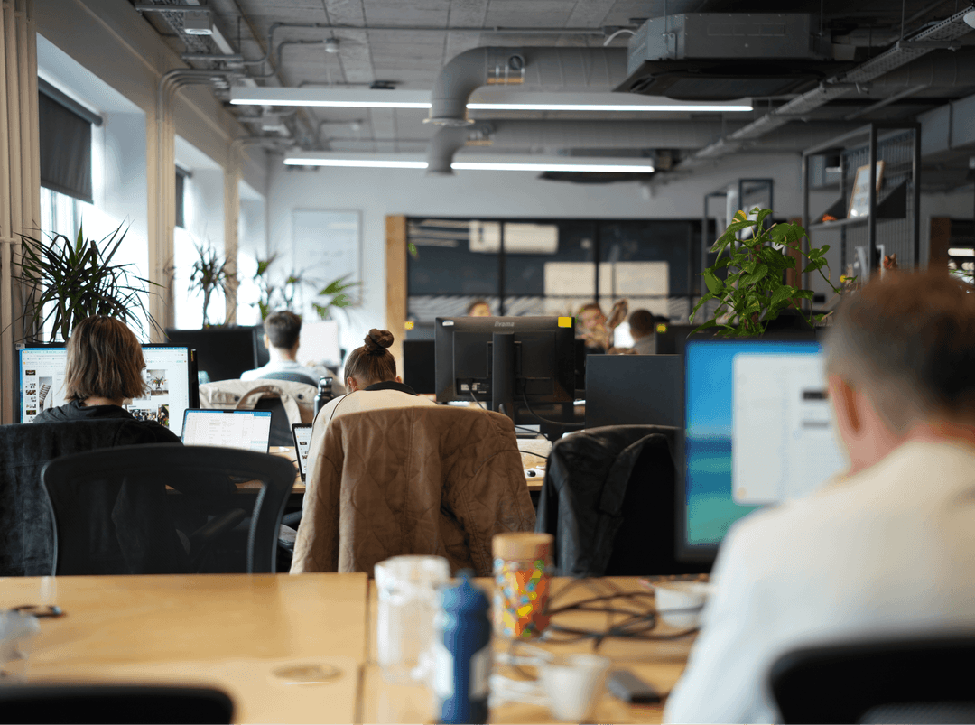Employees working at rows of desks in a spacious, sunlit open-plan office in Manchester.