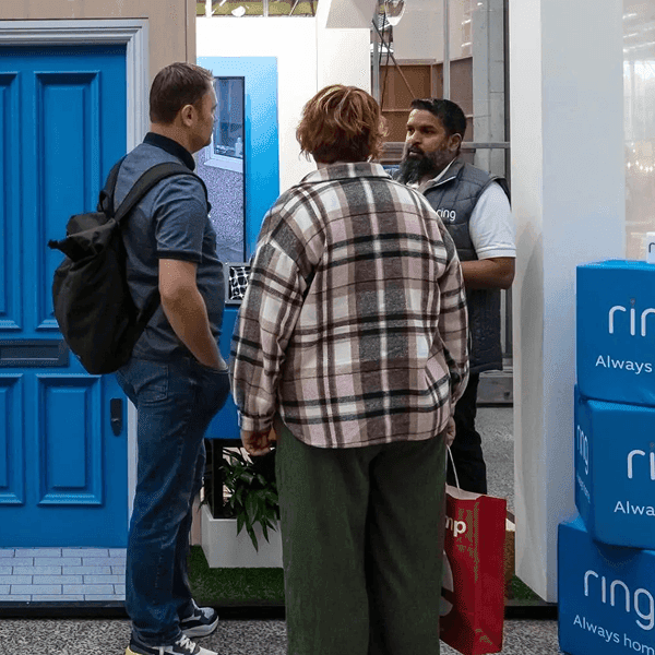 Visitors interacting with a Ring security product display featuring a blue front door prop.