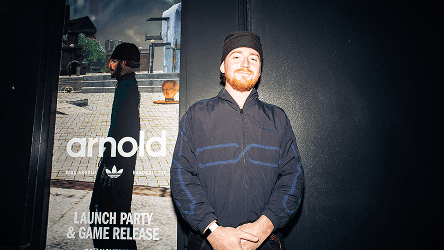 Mike Arnold posing in front of a promotional banner for his Adidas launch party and game release.