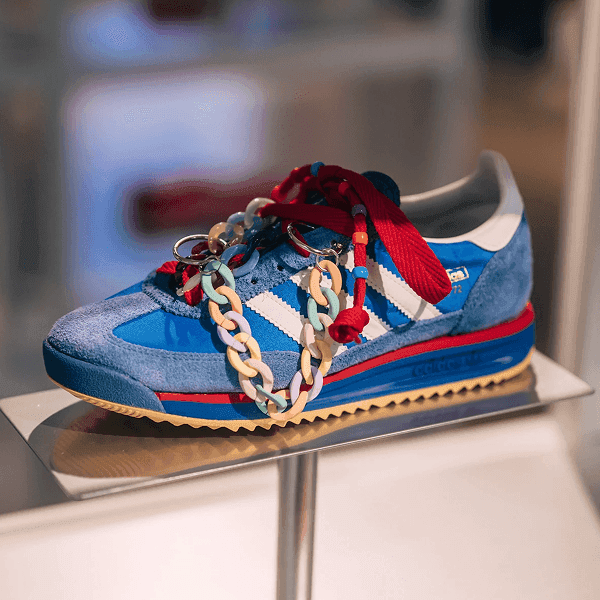 A blue and red Adidas sneaker adorned with a chunky gold chain on a display stand.