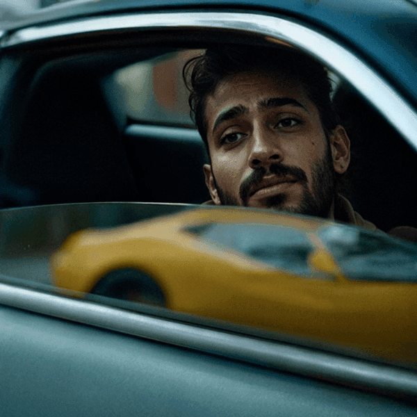 A man looking out of a car window with a yellow vehicle blurred in the reflection.