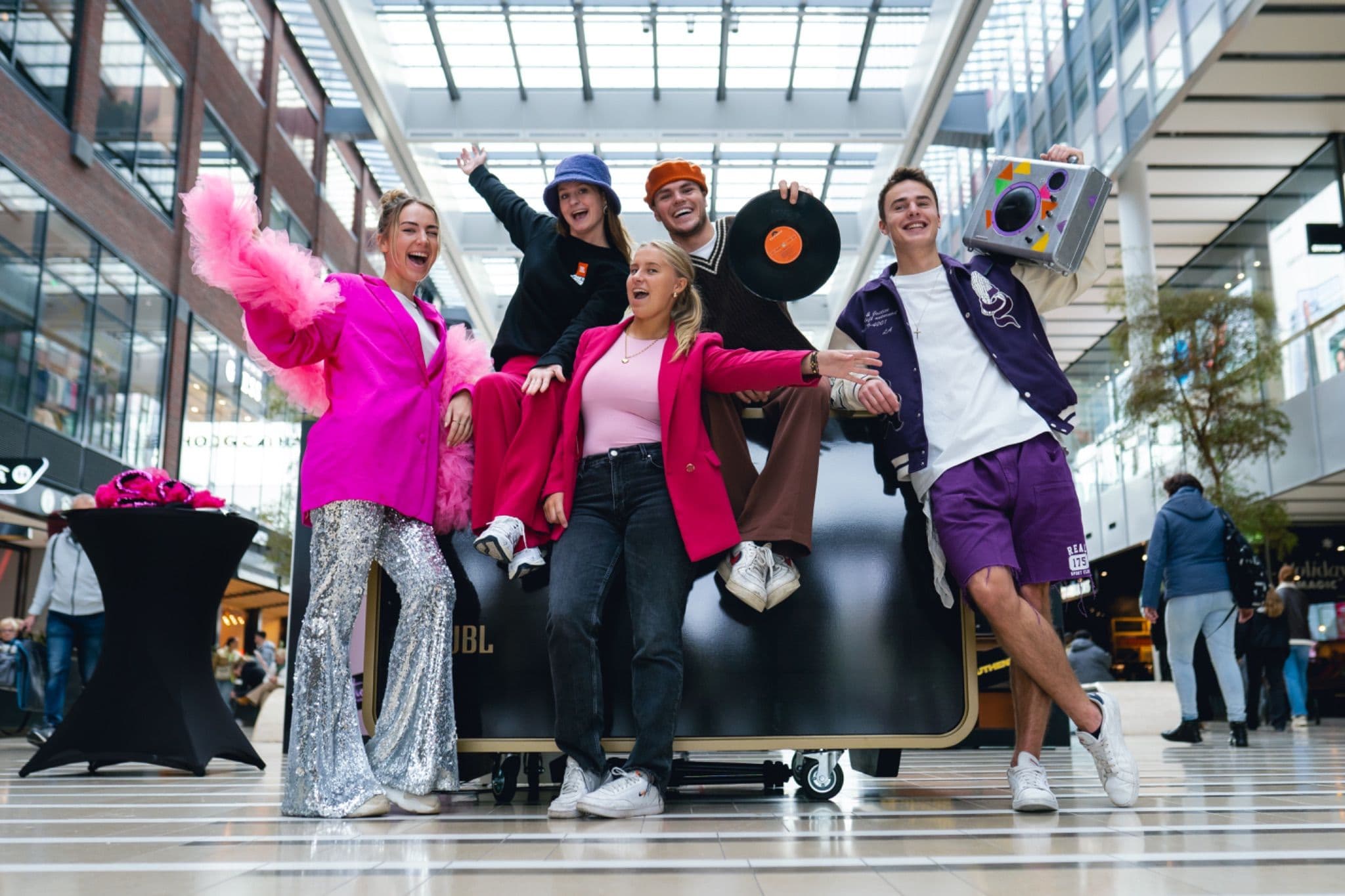Enthusiastic group posing together at a JBL activation, featuring a large retro boombox prop and bright outfits.