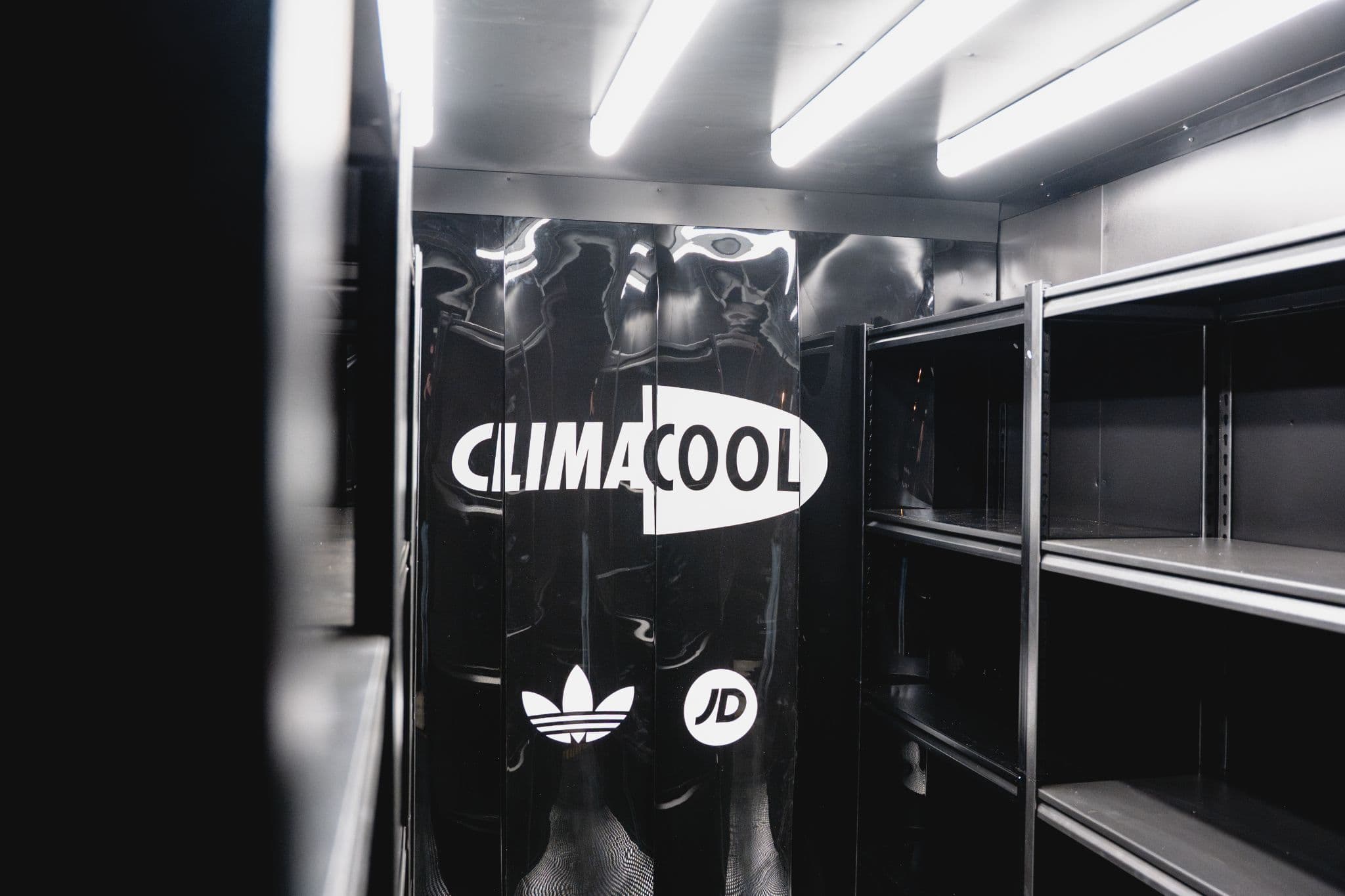 Interior of a delivery truck featuring empty shelves and black walls with Climacool, Adidas, and JD Sports logos.