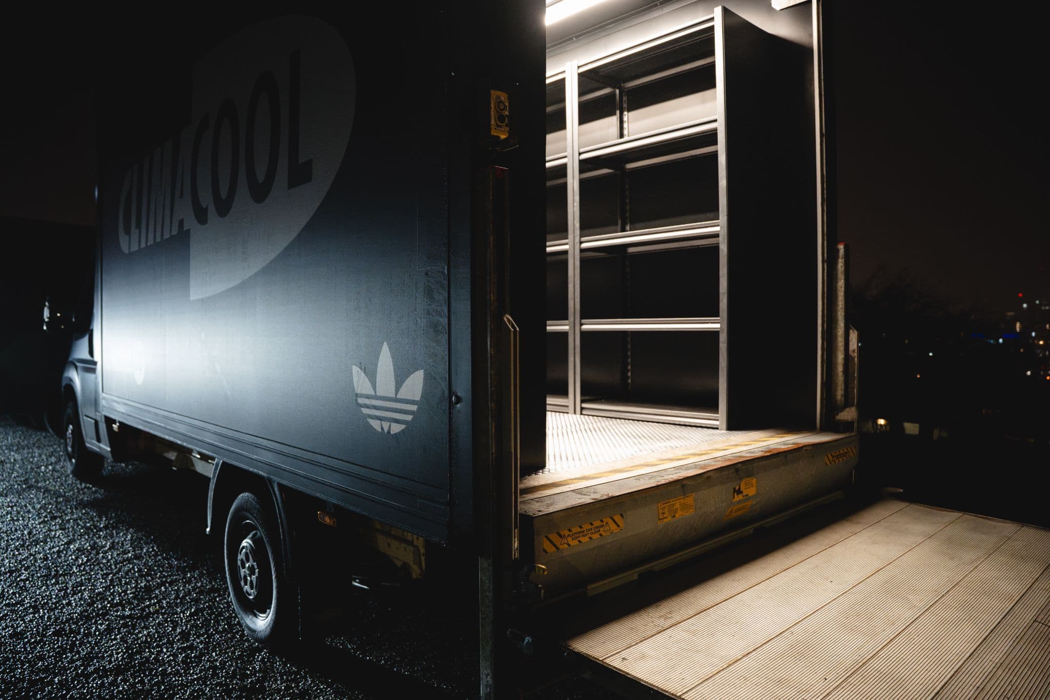 Rear view of an open black Adidas Climacool delivery truck with ramp extended at night.