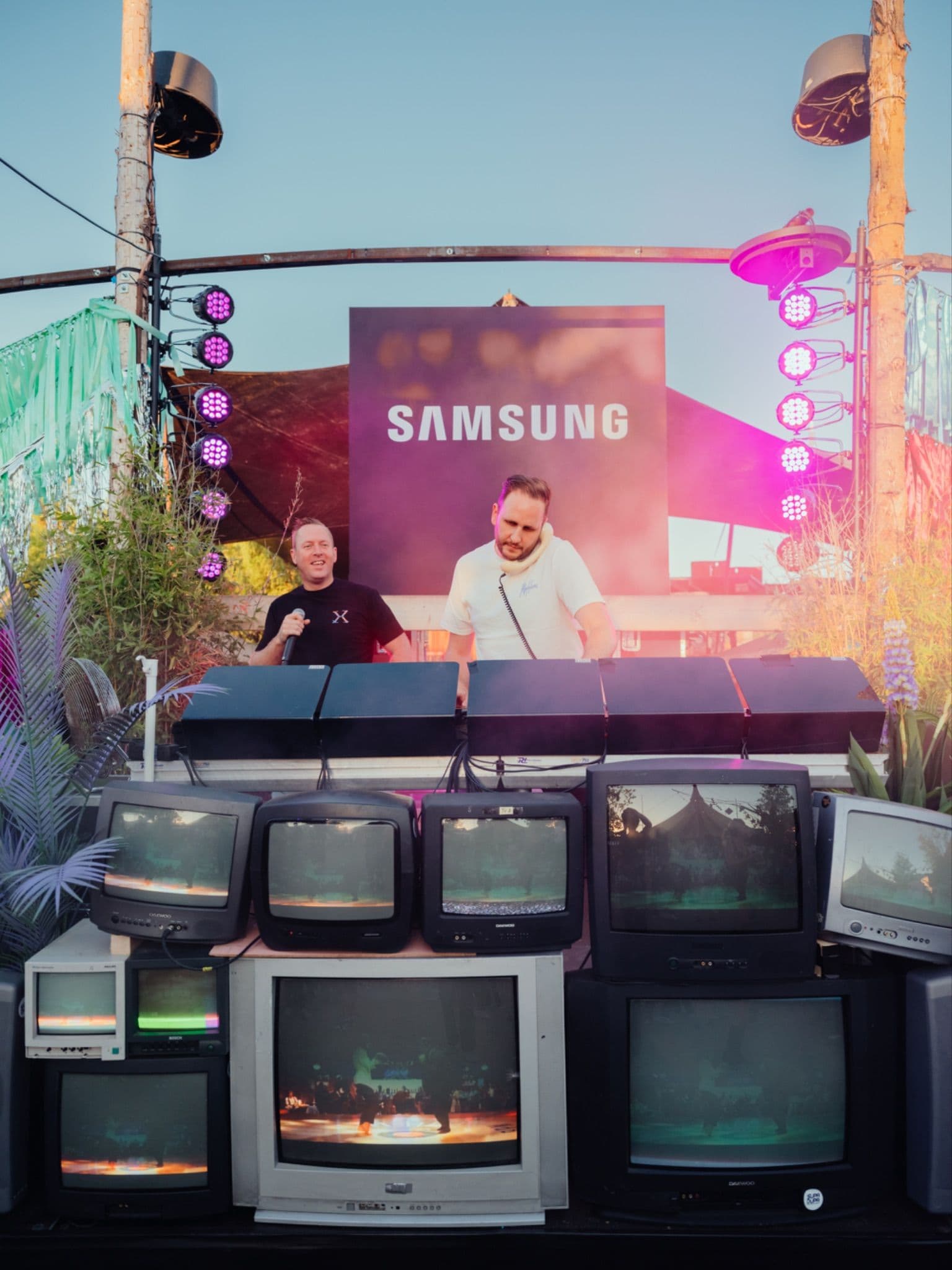 A DJ performing on a stage decorated with a stack of retro CRT televisions under Samsung branding.
