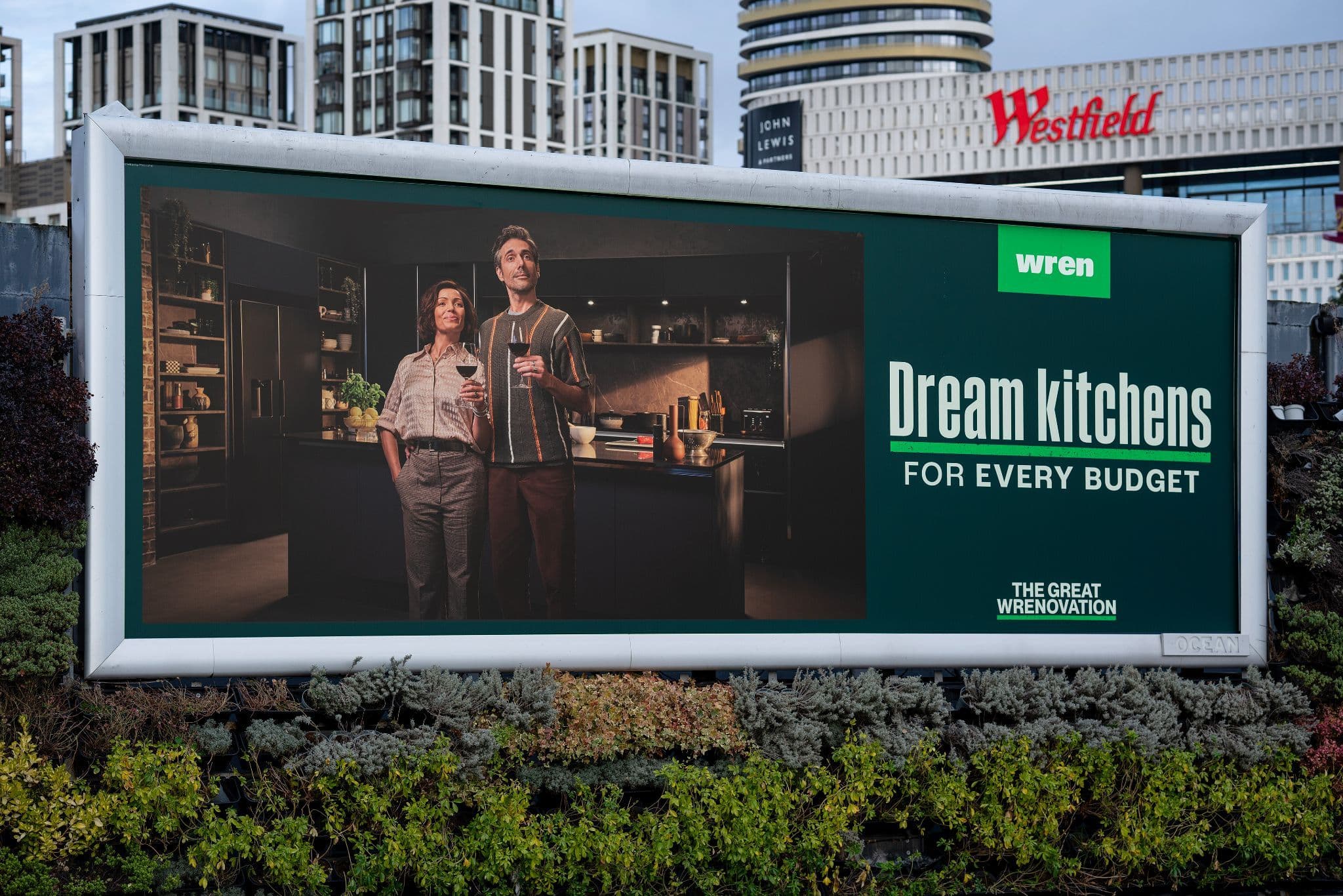 Outdoor billboard featuring a couple in a dark modern kitchen with "Dream kitchens for every budget" text.