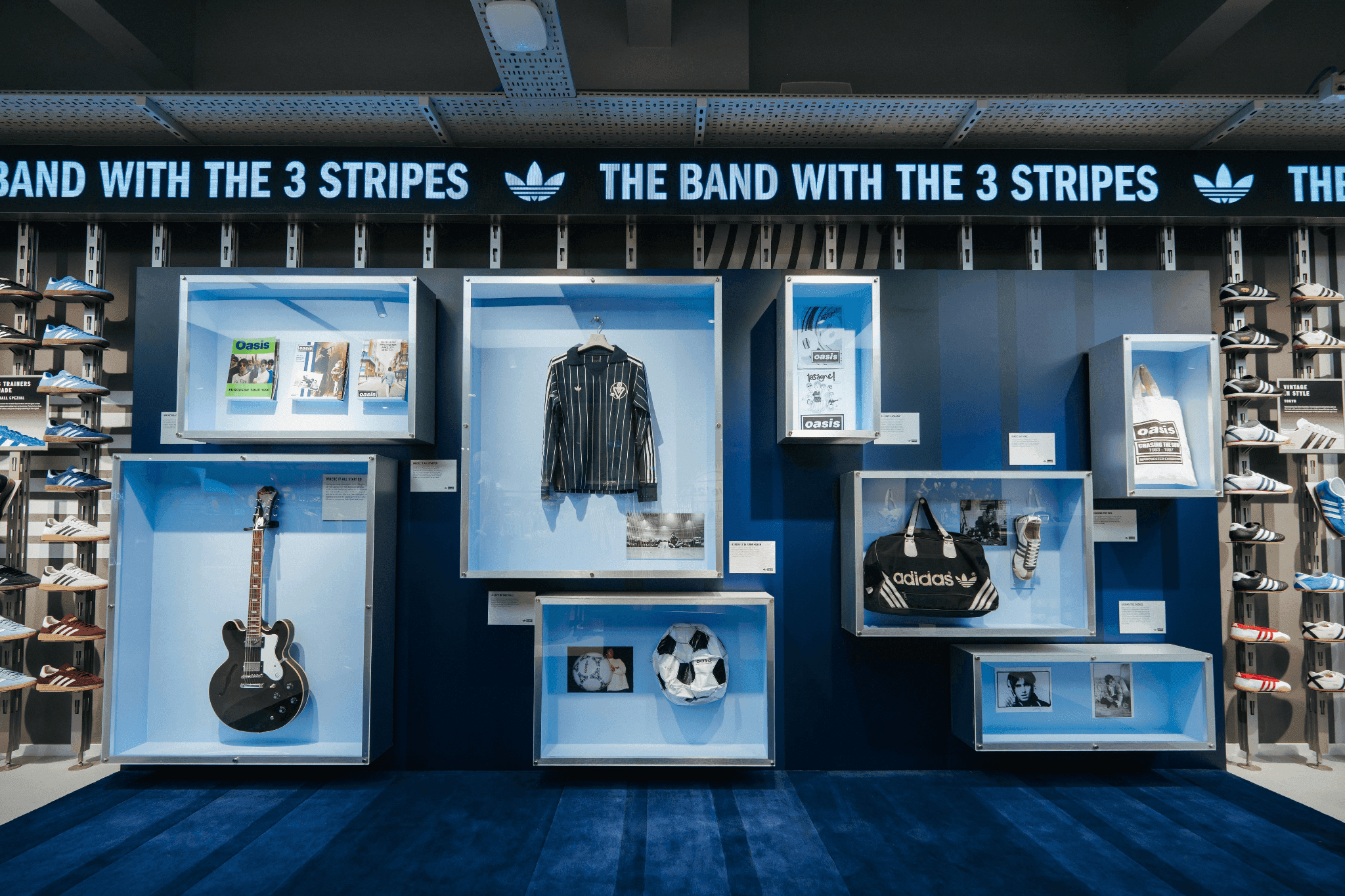 A blue wall display featuring a guitar, jacket, and historical Adidas memorabilia in a retail setting.
