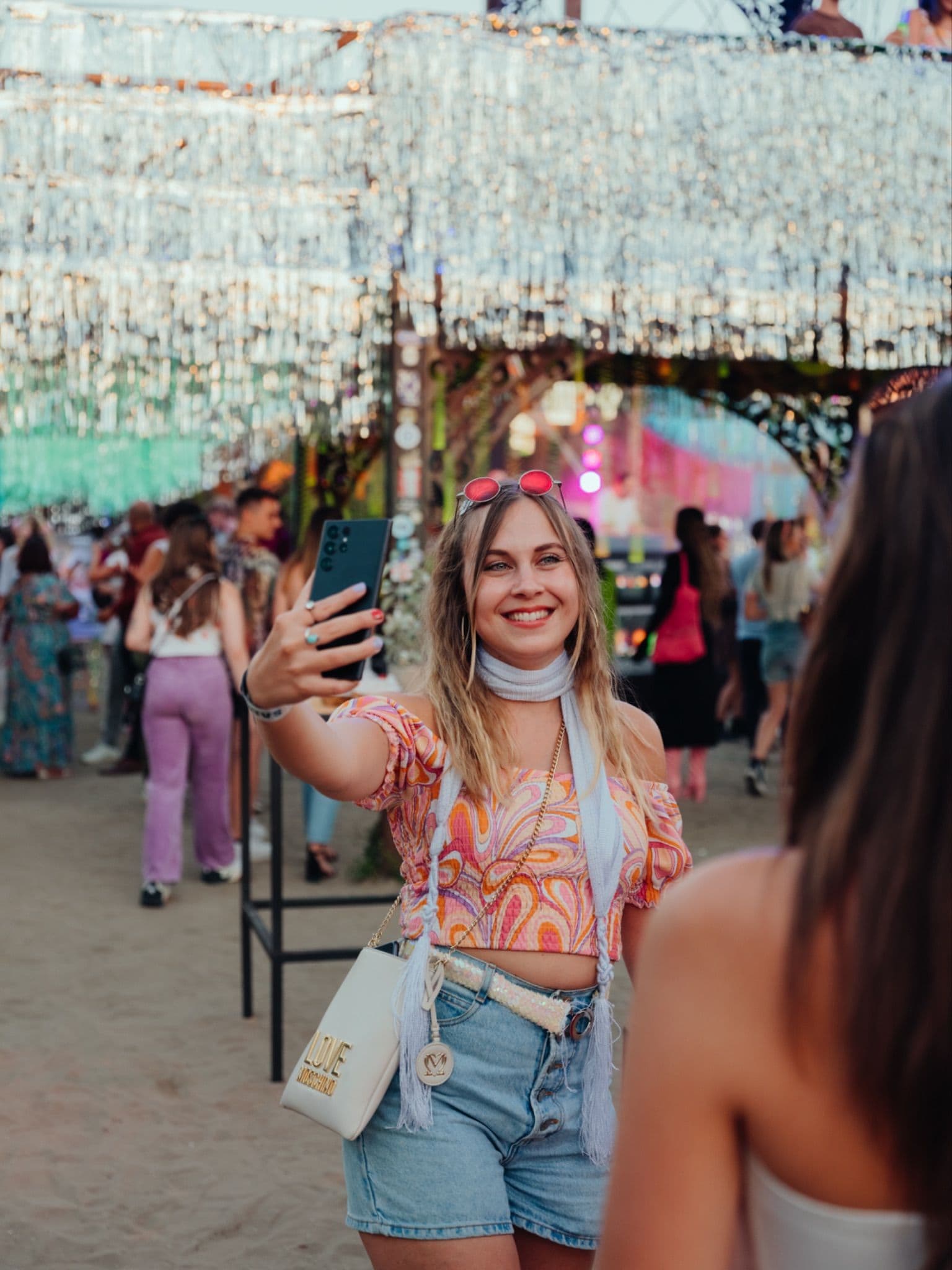 A group of friends taking a selfie and smiling at a crowded outdoor Samsung festival event.