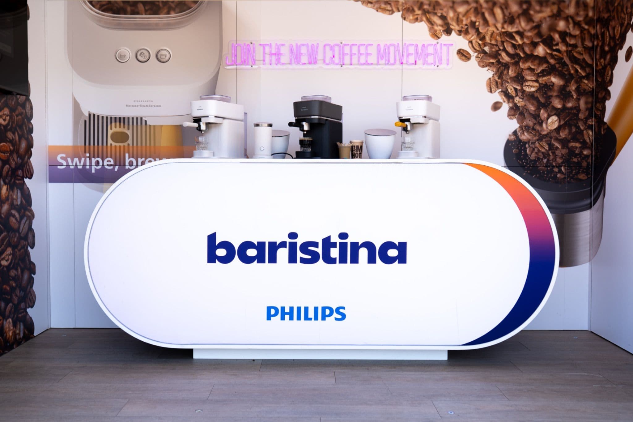 Philips Baristina counter displaying espresso machines with a neon "Join the new coffee movement" sign.