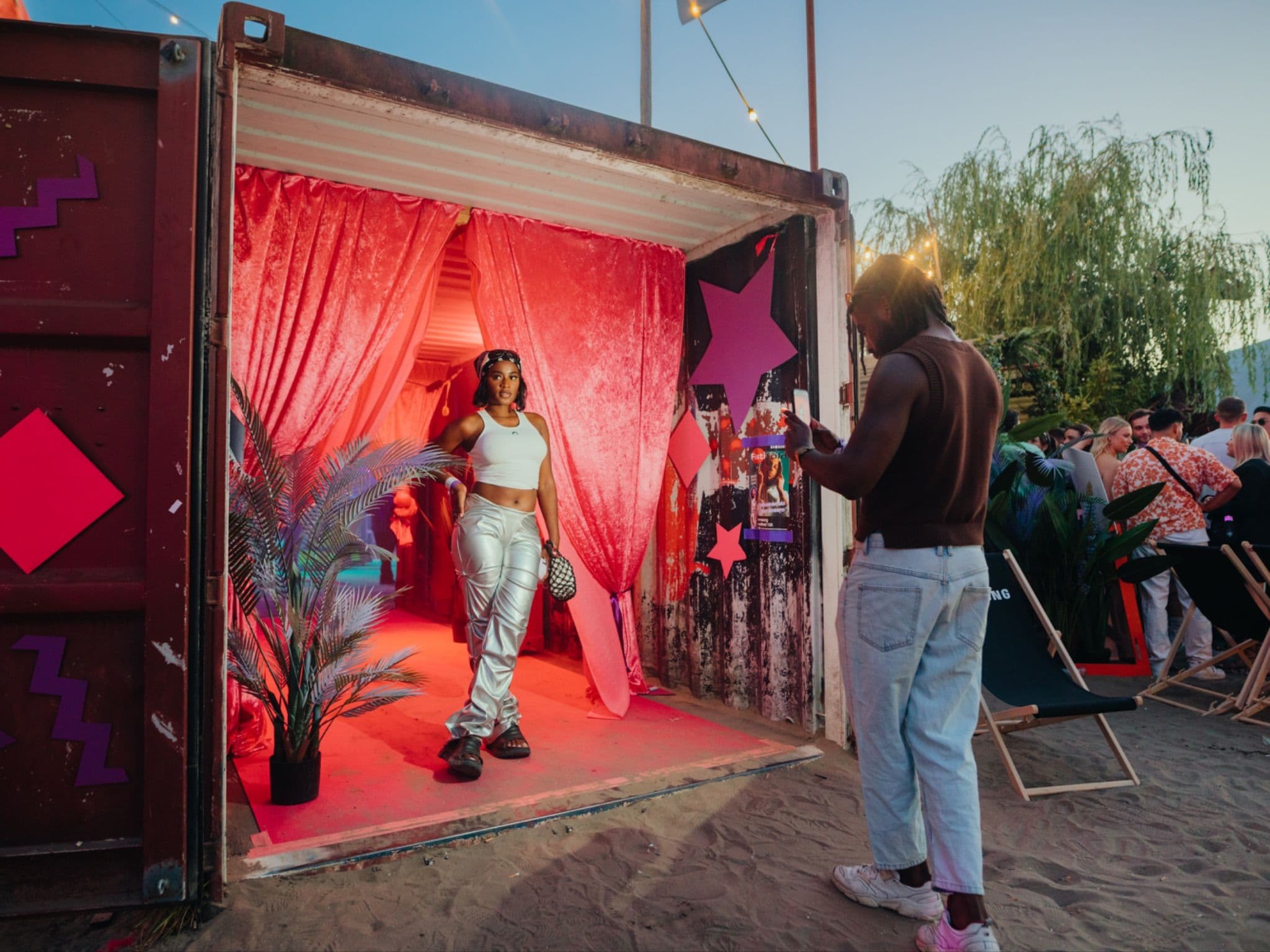 People posing in front of a pink lit Samsung shipping container lounge at an outdoor festival.