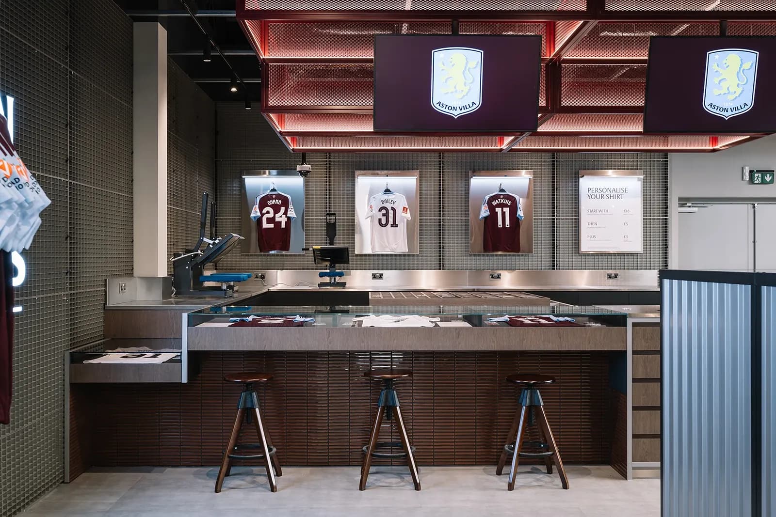 "Personalise Your Shirt" station at Aston Villa store featuring heat press machines and hanging jerseys of Bailey and Watkins.