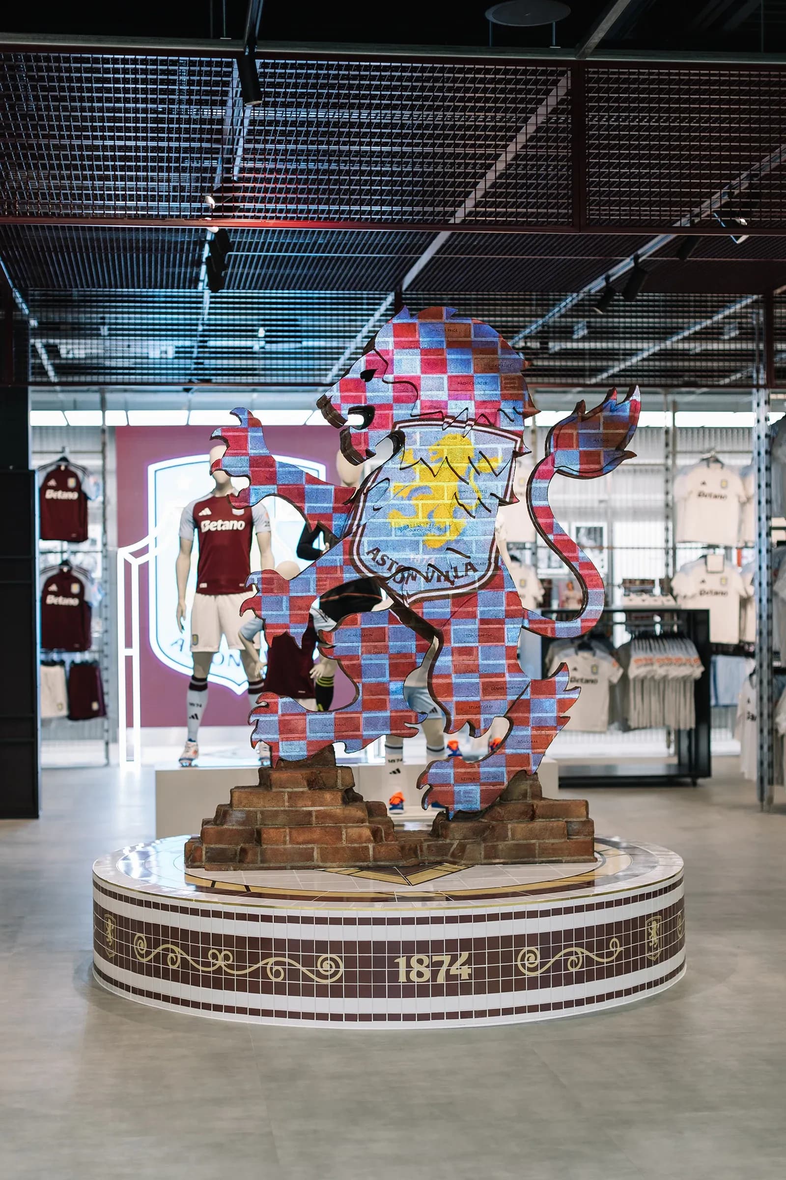 Large lion sculpture covered in a brick pattern featuring the Aston Villa crest, located in the center of the store.