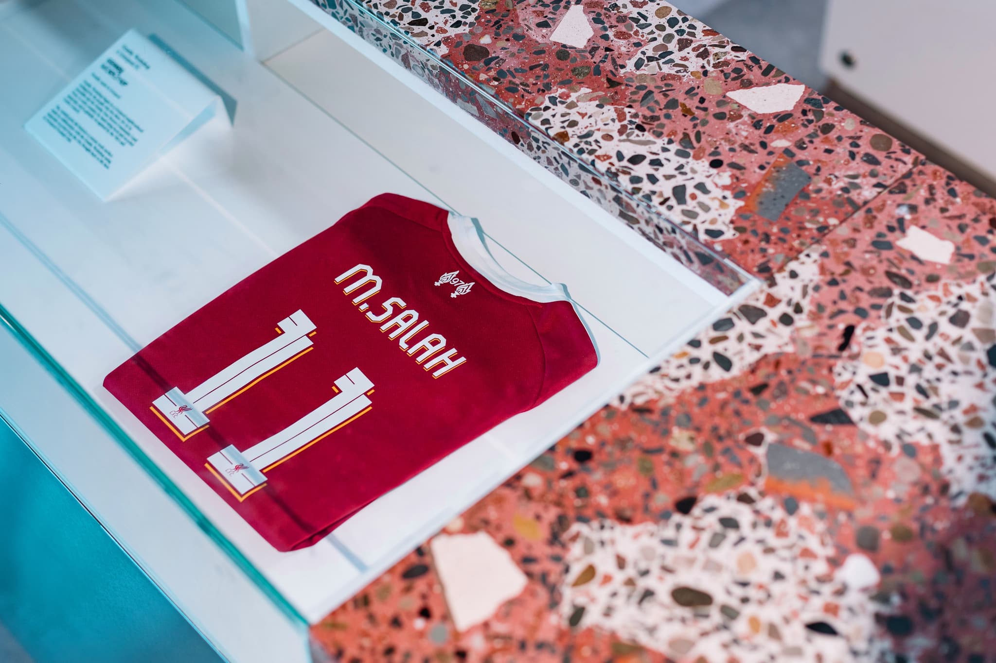 A framed Mohamed Salah number 11 Liverpool jersey inside a museum display case.