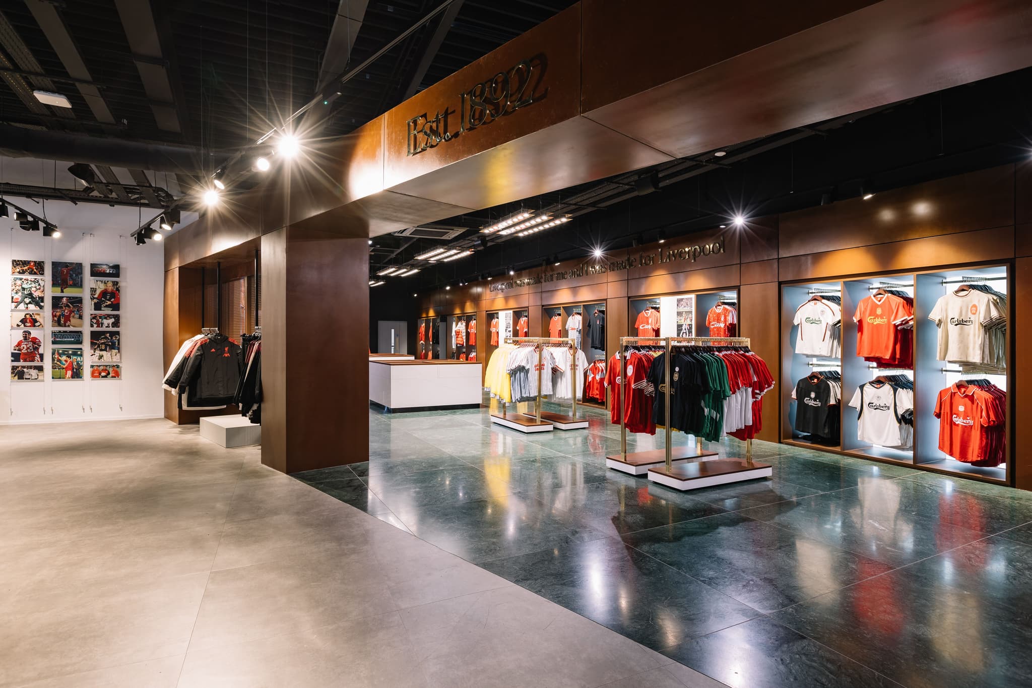 Wide shot of a modern Liverpool FC retail space with wooden partitions and jersey displays.